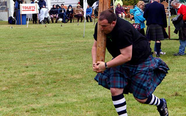 Hombre con kilt lanzando un tronco en juegos de las Tierras Altas en Escocia